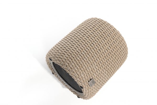 Ein zylindrischer Muffin-Sitzhocker von 4SO in Farbe Latte mit einem dicht gewebten beigen Seil außen, einem flachen schwarzen Sockel und einem kleinen Stoffanhänger ist eine stilvolle Ergänzung für Ihre Gartenmöbel vor einem strahlend weißen Hintergrund.
