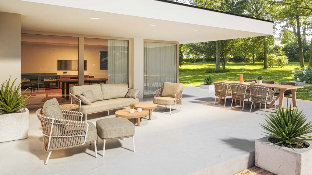 Eine moderne Außenterrasse von 4SO mit beigen Sitzpolstern, einem Sofa, zwei Stühlen, einem niedrigen Holztisch, Topfpflanzen und eleganten Outdoor-Möbeln. Glastüren geben den Blick frei auf einen Innen-Essbereich mit Blick auf üppigen Rasen und Bäume im Hintergrund.