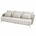 Ein modernes dreisitziges Living-Sofa aus der Serie Beverly von 4SO in Farbe latte, mit hellbeigen und weißen Längsstreifen, Plüschkissen, zwei Wurfkissen und einem leichten Rahmen mit geflochtenen offenen Seiten und leicht angewinkelten Beinen.