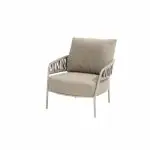 Ein moderner Calma Living-Sessel von 4SO in der Farbe Latte mit hellbeigem Kissen und Polsterung. Das Metallgestell des Stuhls hat Armlehnen mit einem offenen, dekorativen Muster. Sein minimalistisches, neutrales Design eignet sich perfekt als stilvolles Gartenmöbel vor einem schlichten weißen Hintergrund.