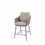 Ein moderner High-Dining-Stuhl in terre aus der Serie Cannes von 4SO mit einem geflochtenen Gestell, Kissen auf Sitz und Rückenlehne, Armlehnen und vier schlanken Metallbeinen mit Fußstützen - perfekt als elegantes Gartenmöbel. Abgebildet vor einem schlichten weißen Hintergrund.