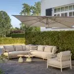 Eine moderne Außenterrasse mit einem großen Modular-Lounge-Sofa, einem passenden Living-Sessel und zwei runden June Couchtischen. Ein großer, freitragender Sonnenschirm spendet Schatten. Entdecken Sie Gartenmöbel bei 1001-Sommer kaufen für Stil wie die Serie Mykonos von 4SO.