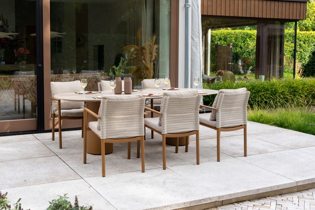 Dining-Stühle aus der Serie Safina von 4SO um einen Colorado Steintisch, der mit Tellern und Vasen auf einer gefliesten Terrasse neben einer Schiebetür steht, hinter der sich üppige Pflanzen und Rasen befinden.