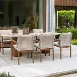 Dining-Stühle aus der Serie Safina von 4SO um einen Colorado Steintisch, der mit Tellern und Vasen auf einer gefliesten Terrasse neben einer Schiebetür steht, hinter der sich üppige Pflanzen und Rasen befinden.